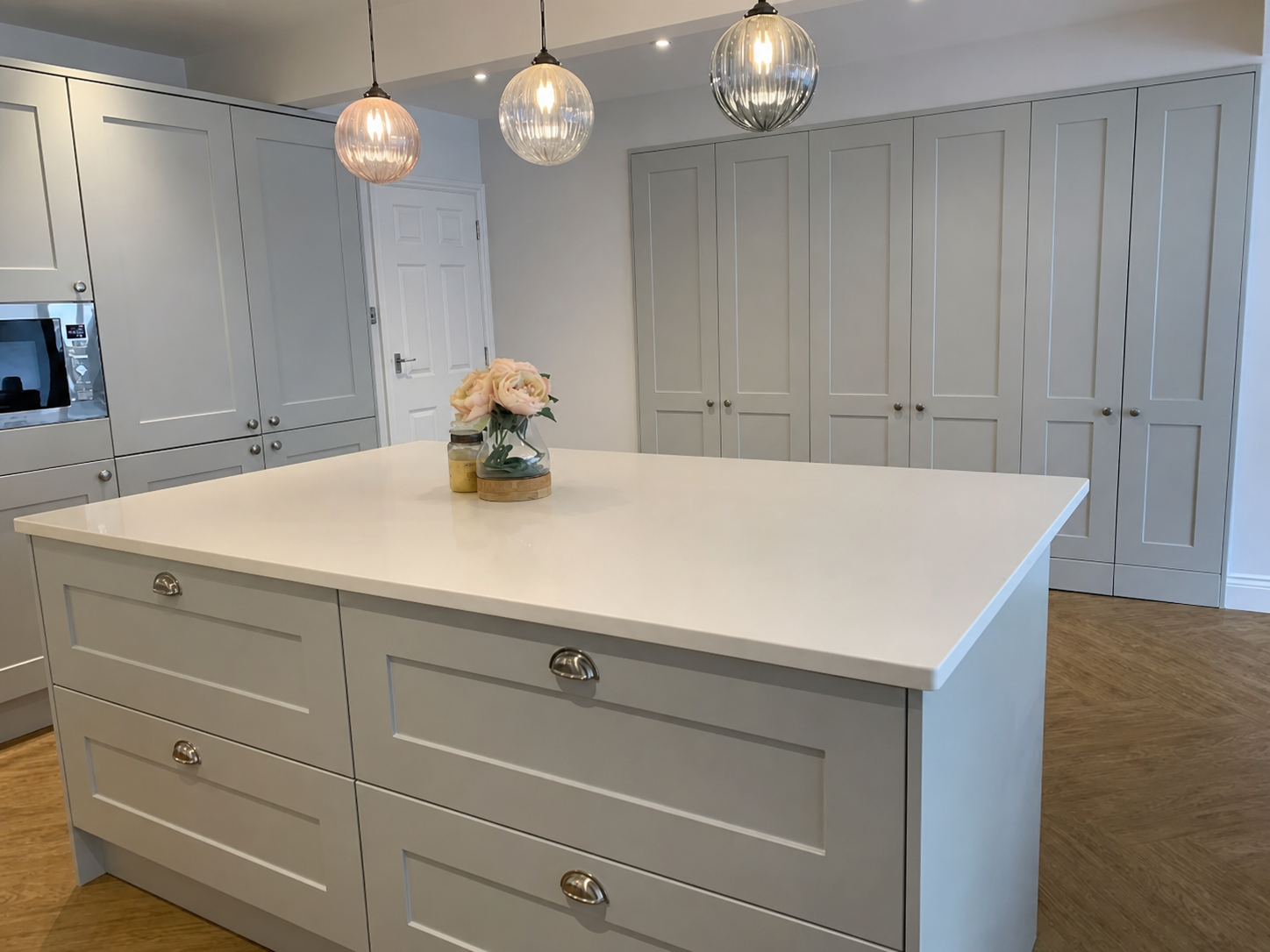 Completed grey shaker kitchen in Basildon with a large white quartz island and glass globe pendant lights
